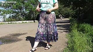 Hairy mature lady struts in a see-through dress outdoors.